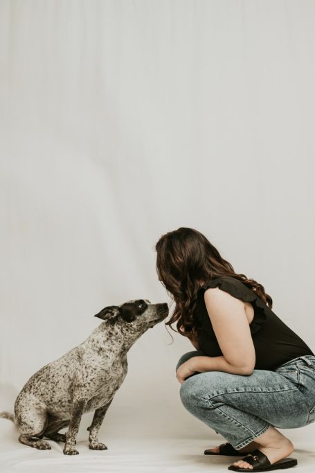 A woman crouches down to greet a dog in a studio setting.